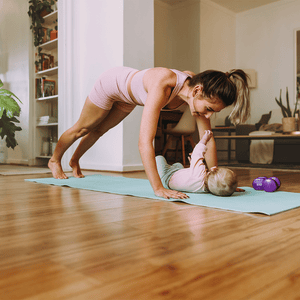 Mama macht Sportübungen auf einer Yoga Matte mit Baby